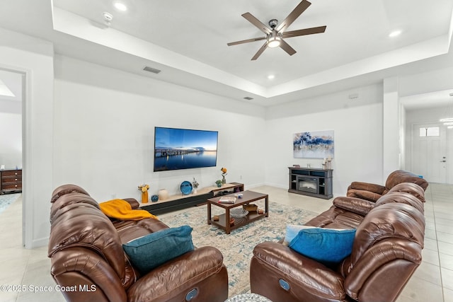 living room featuring a raised ceiling, light tile patterned floors, and ceiling fan