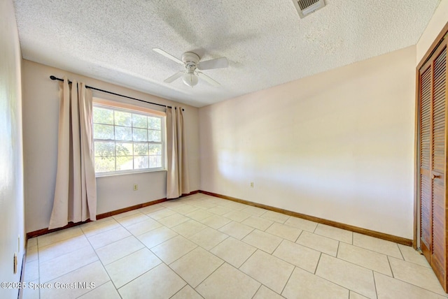 empty room featuring a textured ceiling, light tile patterned flooring, and ceiling fan