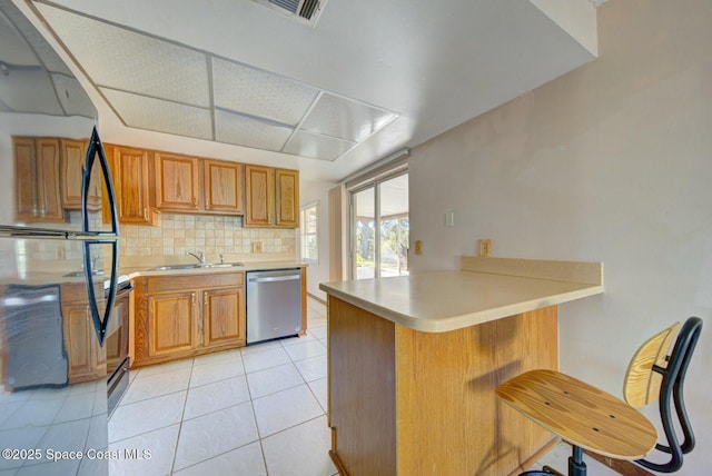 kitchen featuring sink, dishwasher, a kitchen bar, light tile patterned floors, and kitchen peninsula