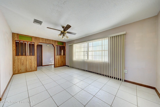 tiled empty room featuring a textured ceiling, wood walls, and ceiling fan