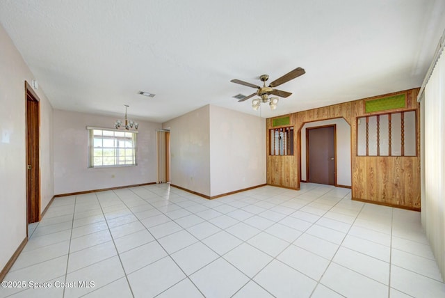 tiled spare room featuring ceiling fan with notable chandelier and wooden walls