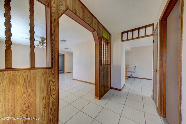 corridor featuring light tile patterned flooring, wood walls, and a textured ceiling