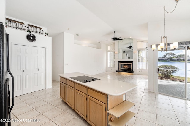 kitchen featuring light tile patterned floors, a water view, a center island, ceiling fan with notable chandelier, and black appliances