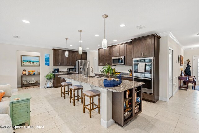 kitchen with decorative light fixtures, dark brown cabinetry, light stone countertops, an island with sink, and stainless steel appliances