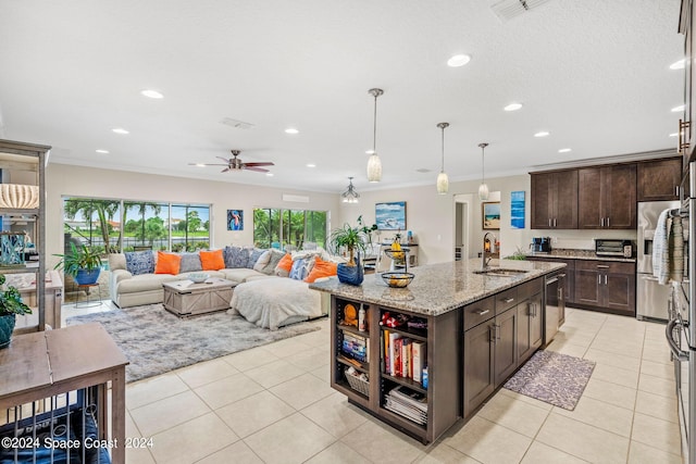 kitchen featuring pendant lighting, sink, an island with sink, dark brown cabinets, and light stone counters