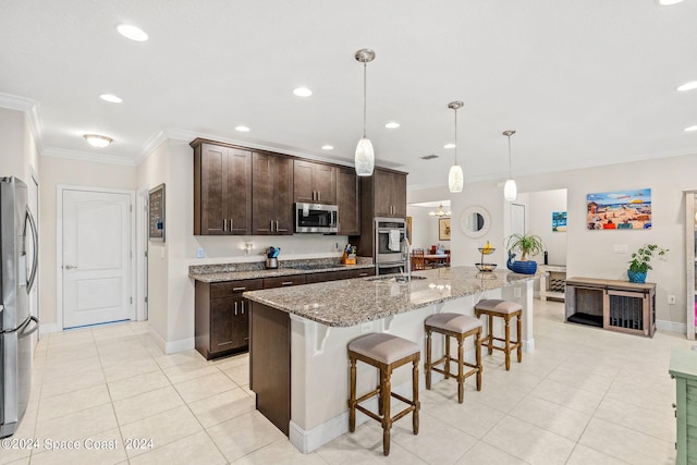 kitchen featuring light stone countertops, stainless steel appliances, an island with sink, hanging light fixtures, and dark brown cabinets