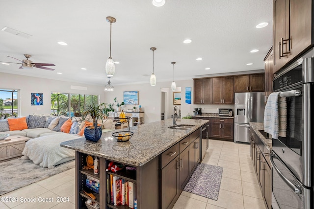 kitchen with decorative light fixtures, dark brown cabinetry, a kitchen island with sink, stainless steel appliances, and light stone counters