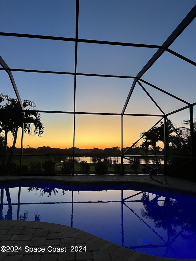 pool at dusk featuring a lanai and a water view