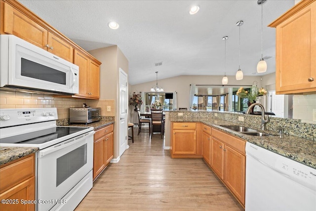 kitchen featuring decorative light fixtures, lofted ceiling, sink, light stone countertops, and white appliances