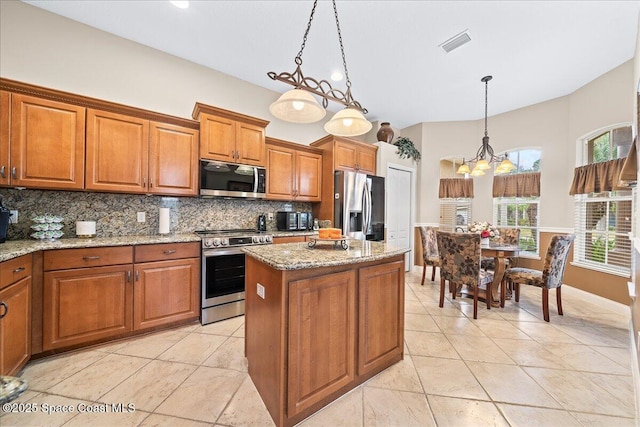 kitchen with pendant lighting, a kitchen island, stainless steel appliances, an inviting chandelier, and light stone counters