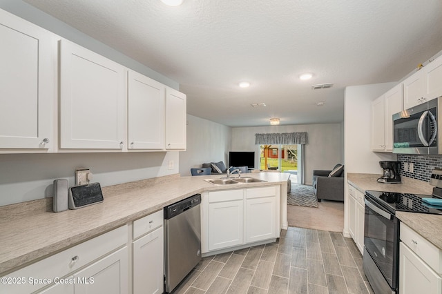 kitchen with a textured ceiling, appliances with stainless steel finishes, white cabinetry, sink, and kitchen peninsula