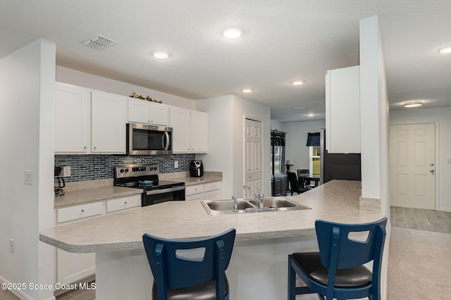 kitchen with kitchen peninsula, sink, appliances with stainless steel finishes, a breakfast bar area, and white cabinets