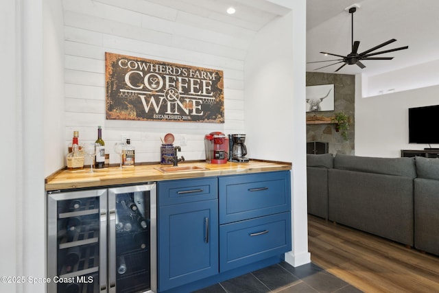 bar with wood counters, beverage cooler, dark hardwood / wood-style flooring, ceiling fan, and blue cabinetry