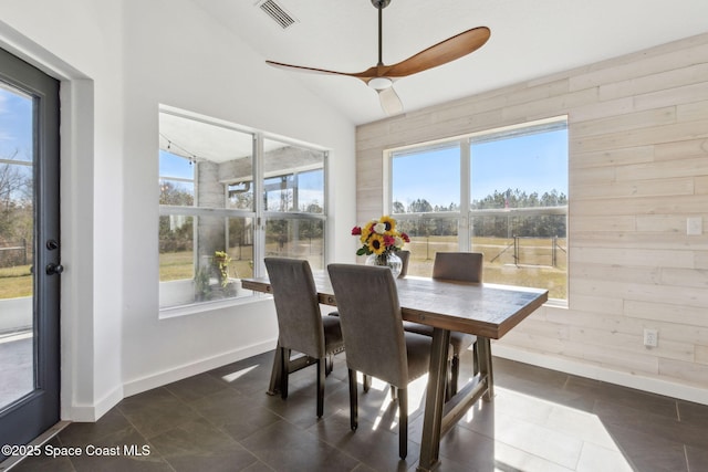 dining space featuring lofted ceiling, plenty of natural light, ceiling fan, and wood walls