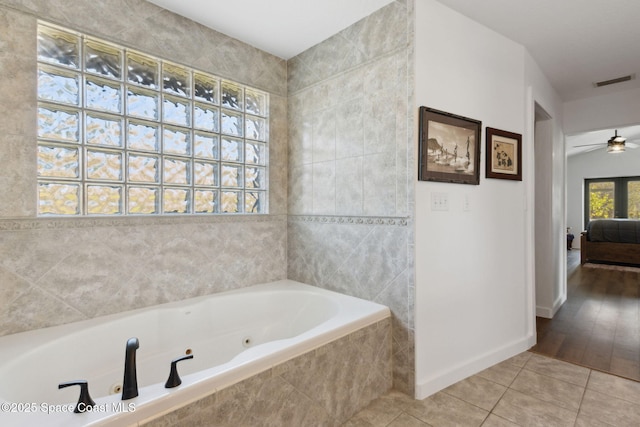 bathroom with tile patterned flooring, tiled tub, and ceiling fan