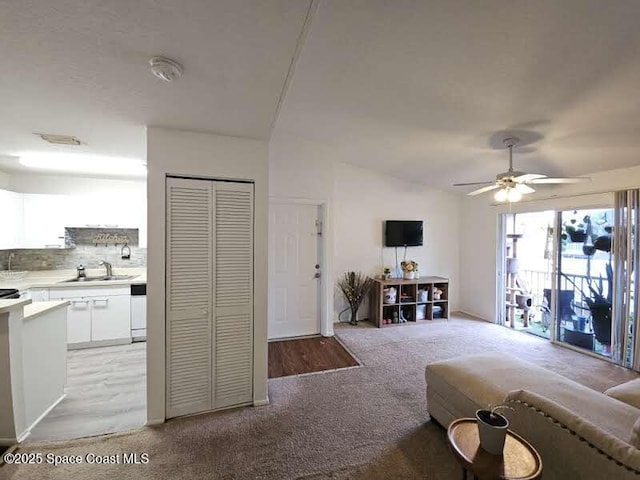 carpeted living room featuring lofted ceiling, sink, and ceiling fan