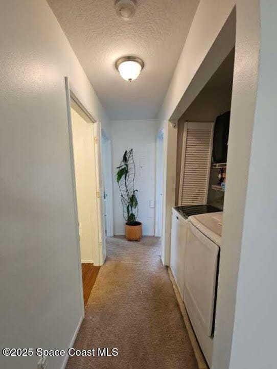 corridor with light colored carpet, separate washer and dryer, and a textured ceiling