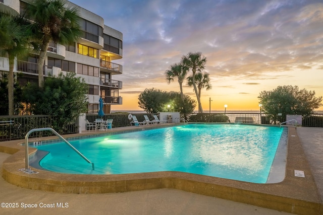 pool at dusk featuring fence and a community pool