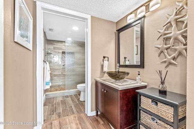 full bathroom featuring toilet, a stall shower, wood tiled floor, vanity, and a textured ceiling