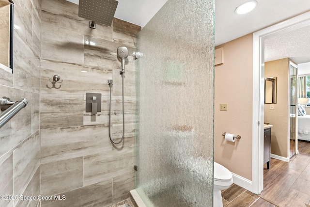 ensuite bathroom with toilet, wood tiled floor, baseboards, and a tile shower