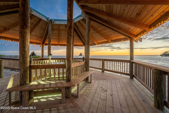 deck at dusk featuring a water view, a view of the beach, and a gazebo