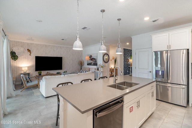 kitchen with a center island with sink, appliances with stainless steel finishes, decorative light fixtures, white cabinets, and sink