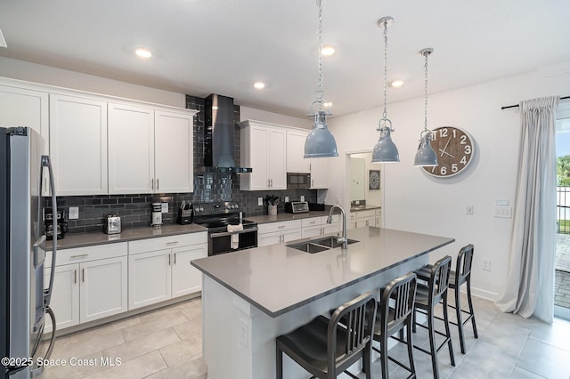 kitchen featuring an island with sink, stainless steel appliances, wall chimney range hood, pendant lighting, and sink