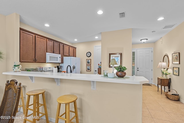 kitchen featuring light tile patterned floors, a kitchen bar, kitchen peninsula, white appliances, and sink