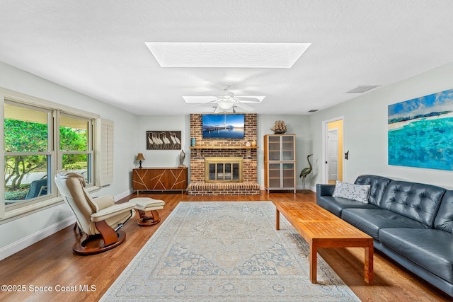 living room with hardwood / wood-style flooring, a brick fireplace, ceiling fan, and a skylight