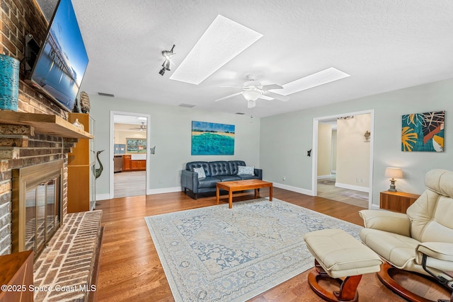 living room featuring a skylight, a textured ceiling, ceiling fan, a fireplace, and light hardwood / wood-style floors