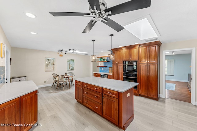 kitchen featuring pendant lighting, a skylight, a center island, light stone counters, and light wood-type flooring