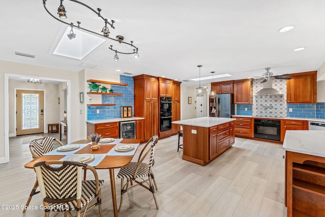 kitchen featuring wall chimney exhaust hood, hanging light fixtures, a kitchen island, beverage cooler, and black appliances