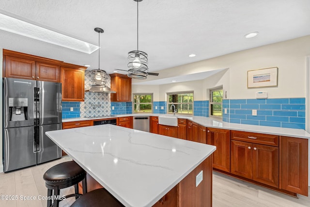 kitchen with hanging light fixtures, stainless steel appliances, a kitchen bar, kitchen peninsula, and wall chimney exhaust hood