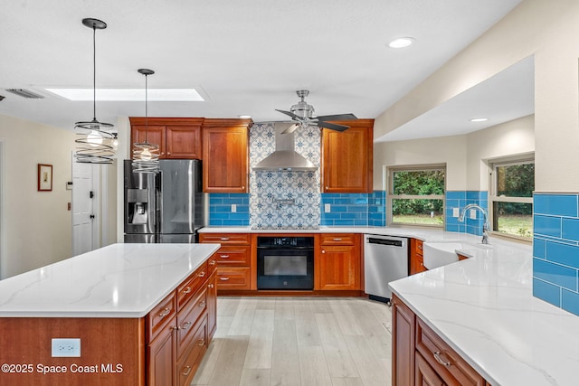 kitchen with sink, light stone counters, black appliances, pendant lighting, and wall chimney range hood