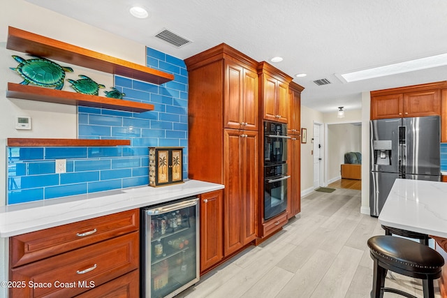 kitchen featuring wine cooler, stainless steel refrigerator with ice dispenser, tasteful backsplash, double oven, and light stone countertops