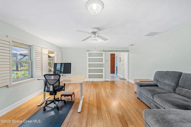 office space with ceiling fan, a barn door, hardwood / wood-style floors, and a textured ceiling