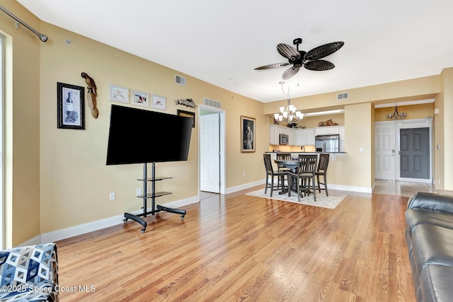 living room with ceiling fan with notable chandelier and light hardwood / wood-style flooring