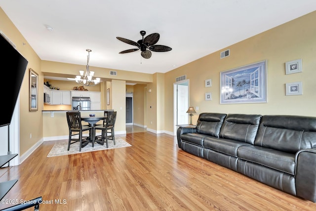 living room with ceiling fan with notable chandelier and light wood-type flooring