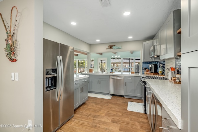 kitchen with sink, gray cabinetry, appliances with stainless steel finishes, light stone countertops, and light hardwood / wood-style floors