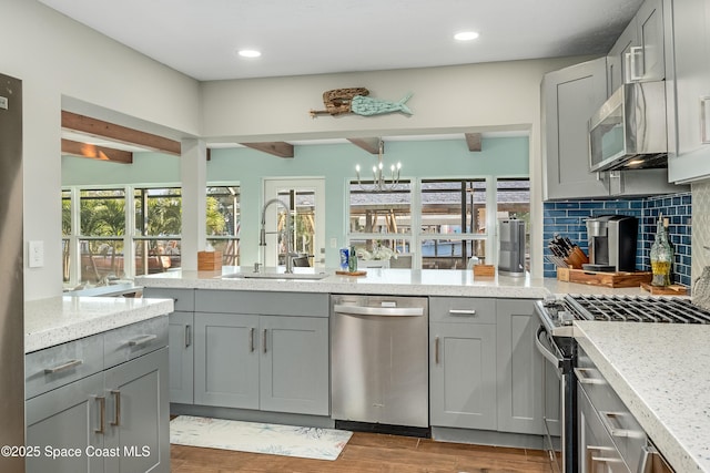 kitchen with stainless steel appliances, light stone countertops, sink, and gray cabinetry