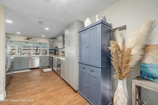 kitchen with stainless steel dishwasher, sink, light hardwood / wood-style floors, and a textured ceiling