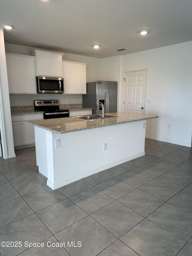 kitchen featuring a sink, white cabinetry, appliances with stainless steel finishes, light stone countertops, and an island with sink