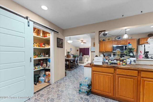 kitchen with ceiling fan, hanging light fixtures, white refrigerator, and a barn door