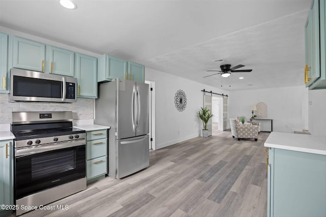 kitchen featuring ceiling fan, a barn door, backsplash, light wood-type flooring, and appliances with stainless steel finishes