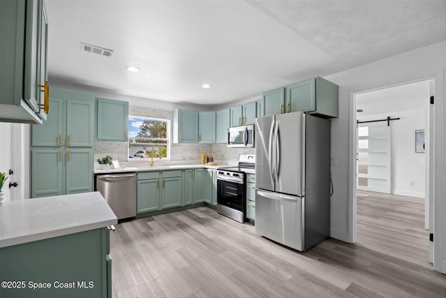 kitchen featuring a barn door, backsplash, appliances with stainless steel finishes, and light hardwood / wood-style flooring