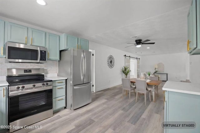 kitchen with ceiling fan, a barn door, backsplash, light wood-type flooring, and appliances with stainless steel finishes