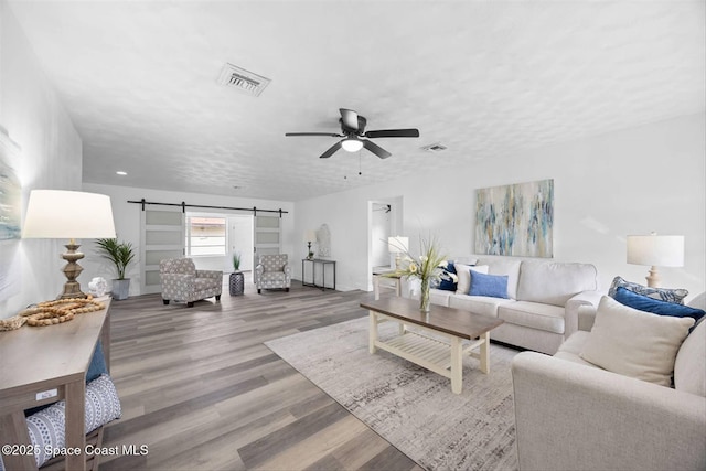 living room with a textured ceiling, ceiling fan, a barn door, and wood-type flooring