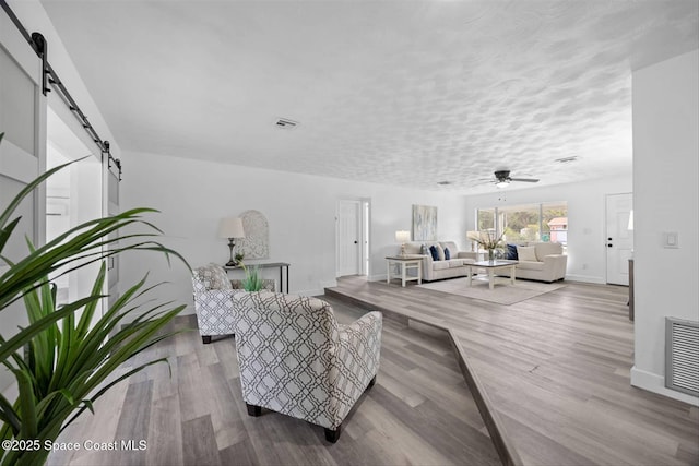 living room featuring ceiling fan, a barn door, light wood-type flooring, and a textured ceiling