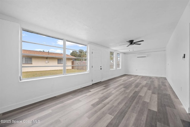 empty room featuring ceiling fan, a wall mounted AC, and light hardwood / wood-style flooring