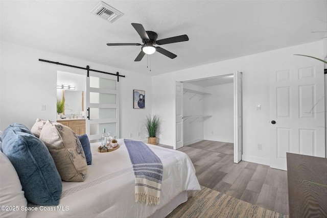 bedroom featuring connected bathroom, ceiling fan, a closet, hardwood / wood-style flooring, and a barn door